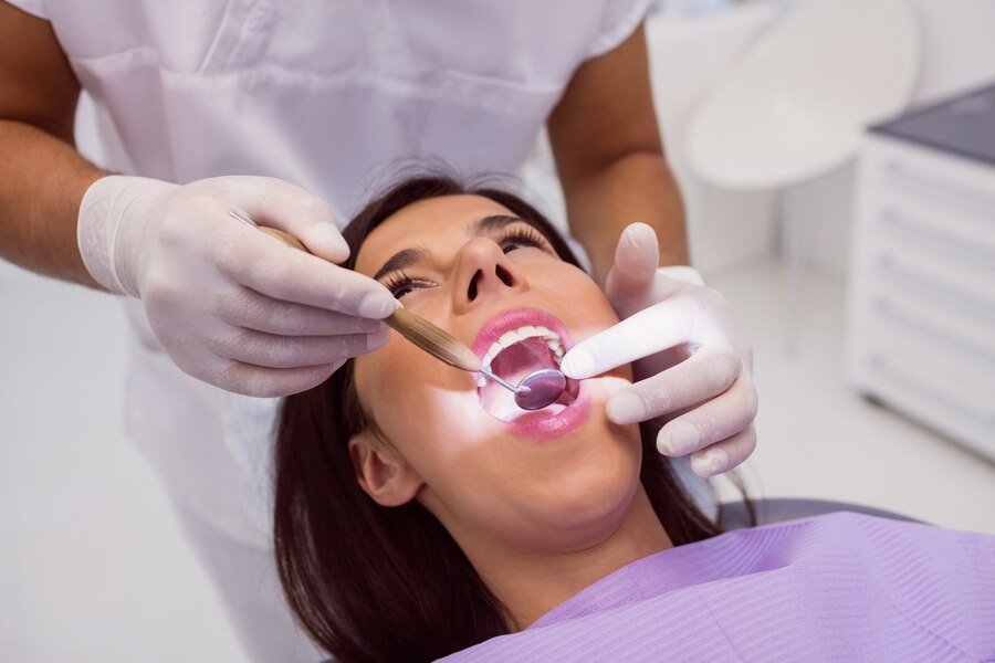 Dental examination of a woman in a dental chair, dentist using a mirror and light to assess oral health, focused on TMJ treatment at Harborside Dental in Gloucester, MA.