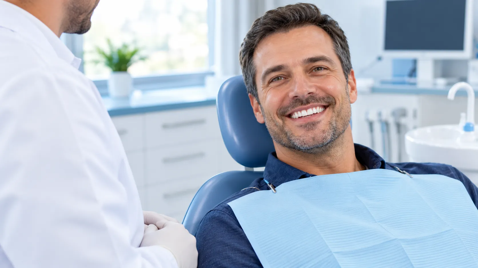 Smiling man with healthy white teeth in a blue dental chair, with a dentist beside him after a tooth-colored filling check
